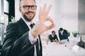 handsome young businessman showing okay sign with blurred colleagues Royalty Free Stock Photo