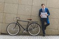 handsome young businessman in stylish suit with bicycle reading newspaper leaning Royalty Free Stock Photo