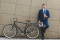 handsome young businessman in stylish suit with newspaper and bicycle leaning Royalty Free Stock Photo