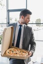 handsome young businessman in suit holding box with pizza