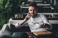 Handsome young businessman talking on mobile phone and drinking coffee in outdoor cafe Royalty Free Stock Photo