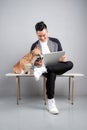 Handsome young businessman is using laptop while sitting with his dog on chair Royalty Free Stock Photo