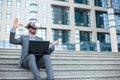 Young businessman using VR goggles and making hand gestures, working on a laptop in front of an office building Royalty Free Stock Photo