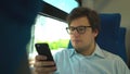 Handsome young businessman wearing a blue shirt and glasses is riding a train dialing a number and talking on his phone