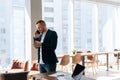 Handsome young businessman wearing fashion suit is talking on mobile phone in modern office room Royalty Free Stock Photo