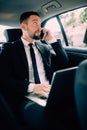 Handsome young businessman working on his laptop and talking on the phone while sitting in the car Royalty Free Stock Photo