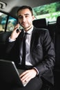 Handsome young businessman working on his laptop and talking on the phone while sitting in the car Royalty Free Stock Photo