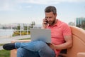Handsome young businessman working with laptop outdoors talking on mobile phone. Royalty Free Stock Photo