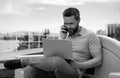 Handsome young businessman working with laptop outdoors talking on mobile phone. Royalty Free Stock Photo