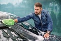 Handsome young Caucasian man cleaning his car windshield with green sponge mitten and soap foam outdoors at car wash Royalty Free Stock Photo