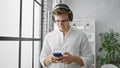 Handsome young caucasian man, a confident business executive, engrossed in work at the office, joyfully listening to music on his Royalty Free Stock Photo