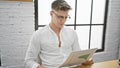 Handsome young caucasian man, a focused office worker, engrossed in reading a business document at his desk, with an air of Royalty Free Stock Photo