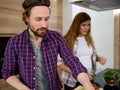 Handsome young Caucasian man preparing meal with her pregnant woman out of focus on the background at home kitchen