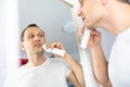 Handsome young man is shaving with electric razor while looking at the mirror. Royalty Free Stock Photo