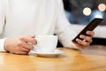 Handsome young caucasian man sitting at cafe using mobile phone and having coffee. Caucasian male with cup of coffee and