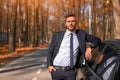 A handsome young Caucasian man wearing business suit standing near black car on nature Royalty Free Stock Photo