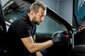 Handsome young Caucasian man, worker of professional car detailing workshop, cleaning car door interior by a soft brush Royalty Free Stock Photo