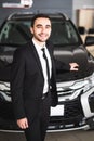 Handsome young classic car salesman standing at the dealership in front of new car Royalty Free Stock Photo