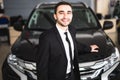 Handsome young classic car salesman standing at the dealership in front of new car Royalty Free Stock Photo