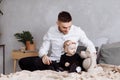 Handsome young dad and his cute baby girl are sitting and playing with teddy bear on bed at home. father`s, baby`s day. family Royalty Free Stock Photo