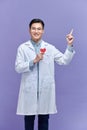 Handsome young doctor man holding paper with red heart, very happy pointing with hand and finger Royalty Free Stock Photo