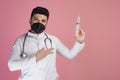 Handsome, young doctor wearing mask, looking at camera, raising hand, showing syringe. Royalty Free Stock Photo
