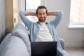 Handsome young European man with beard sitting on the sofa with laptop at home, searching in the internet, watching film Royalty Free Stock Photo
