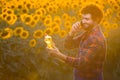 Handsome young farmer standing in the middle of a golden sunflower field smiling and talking on phone while holding up a sunflower Royalty Free Stock Photo