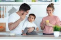 Handsome young father feeding his baby son while the mother looking them in the kitchen at home Royalty Free Stock Photo