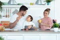 Handsome young father feeding his baby son while the mother looking them in the kitchen at home Royalty Free Stock Photo