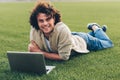 Handsome young freelance businessman sitting on the ground, working on laptop. Smiling man with curly hair using laptop for Royalty Free Stock Photo