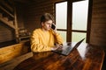 Handsome young freelancer man working in a wooden country house on a laptop and calling by phone. Freelancer working on a laptop Royalty Free Stock Photo