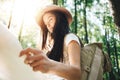 Handsome young girl traveling among trees in forest at sunset. Woman wearing backpack and hat hold in hands location map