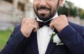 Handsome young groom fixing bow tie outdoors, closeup