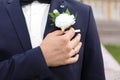 Handsome young groom fixing buttonhole outdoors, closeup