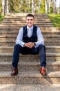 Handsome young groom wearing elegant and stylish dark blue suit outdoors portrait. Happy groom sitting on stairs.