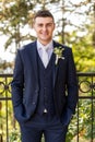 Handsome young groom wearing elegant and stylish dark blue suit outdoors portrait. Happy groom looking and smiling at camera. Royalty Free Stock Photo