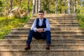 Handsome young groom wearing elegant and stylish dark blue suit outdoors portrait. Stylish groom sitting on stairs. Royalty Free Stock Photo