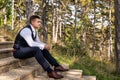 Handsome young groom wearing elegant and stylish dark blue suit outdoors portrait. Stylish groom sitting on stairs side view.