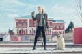 A handsome young guy in a khaki and berets military coat walks with a big dog. Holds a flask in his hand