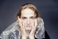 A handsome young guy with long blonde hair and sad blue eyes holds a bubble wrap in front of his face Royalty Free Stock Photo