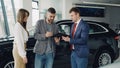 Handsome young guy signing sale and purchase agreement in car dealership Royalty Free Stock Photo