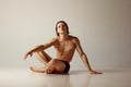 Handsome young guy with sportive, muscular body sitting on floor, posing shirtless in underwear against grey studio Royalty Free Stock Photo