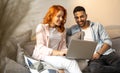 Handsome, young and happy couple watching movie together on a laptop while sitting cuddled up on the sofa at home. Royalty Free Stock Photo