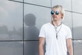 Handsome young hipster blond man in blue round sunglasses with stylish hairstyle in a trendy white t-shirt with amulets is Royalty Free Stock Photo