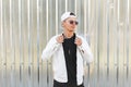 Handsome young hipster fashionable man in dark sunglasses in a stylish white jacket in a trendy baseball cap in a black t-shirt Royalty Free Stock Photo