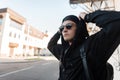 Handsome young hipster man in a hooded sweatshirt in a baseball cap in sunglasses with a backpack is standing Royalty Free Stock Photo