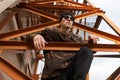 Handsome young hipster man in knitted hat in camouflage shirt in sunglasses posing sitting on an iron orange staircase outdoors Royalty Free Stock Photo