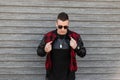 Handsome young hipster man in a stylish plaid jacket in a trendy black t-shirt with black sunglasses