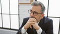 Handsome young hispanic grey-haired man exuding confidence, sitting in a relaxed manner at his indoor office, engrossed in deep Royalty Free Stock Photo